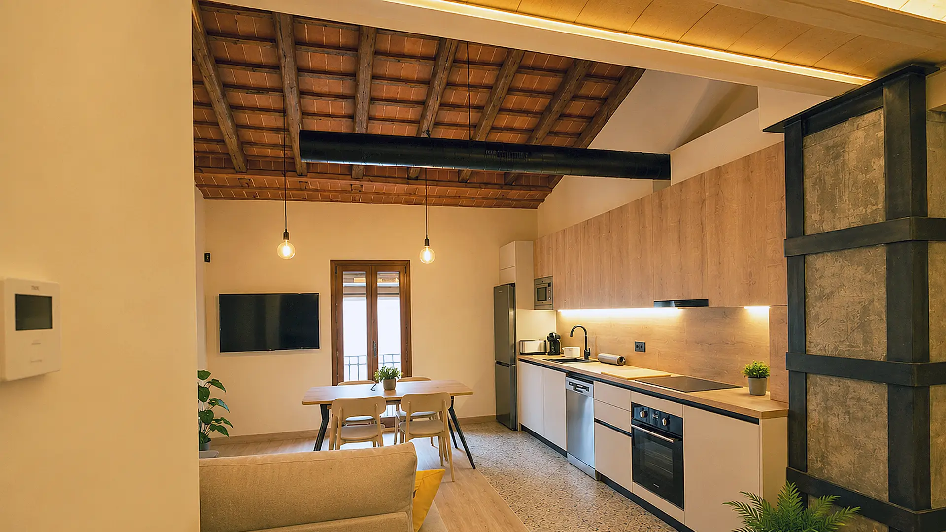 Interior de l'apartament Ametlla Tarraco amb sostre de fusta i cuina oberta